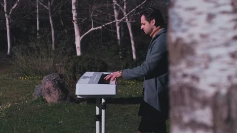 Elegant man playing white digital piano outdoors in cinematic garden setting Stock Footage 334628893