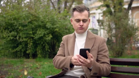 Elegant man uses smartphone while sitting on a bench on the street. Business Stock Footage 144885751