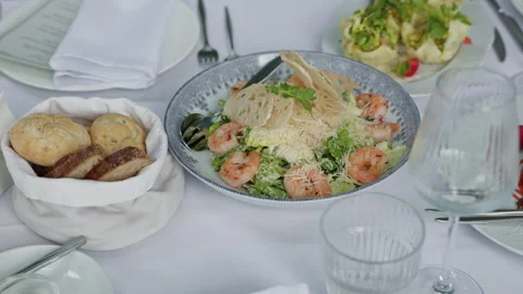 Elegant seafood salad dinner table with shrimp, bread basket, white linens Stock Footage 337648313