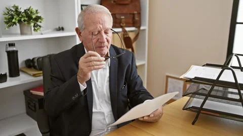 Elegant senior man focused at work, reading business document, taking off g.. Stock Footage 261379396