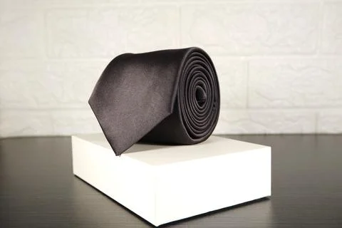 Elegant solid black color polyester fabric necktie rolled over white background Stock Photos