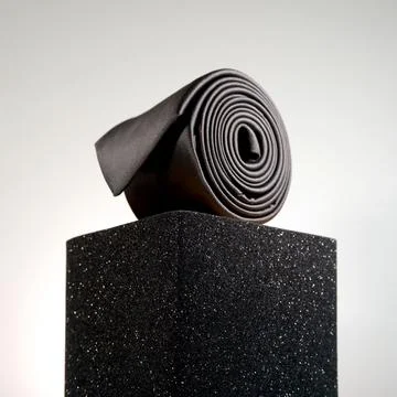 Elegant solid black color polyester fabric necktie rolled over white background Stock Photos