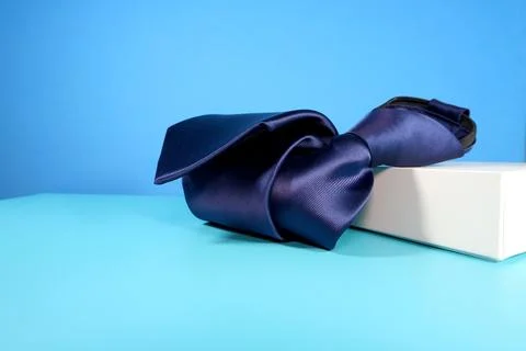 Elegant solid striped blue polyester fabric necktie rolled over blue background Stock Photos