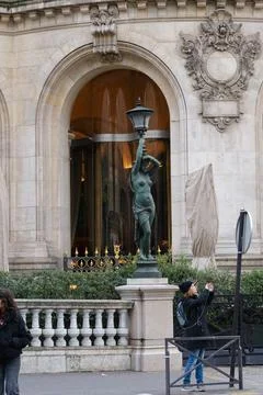 Elegant statue holding a lamp post stands outside a historic building in a .. Stock Photos