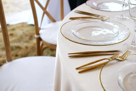 Elegant wedding table setting with gold cutlery and clear plates, featuring soft Stock Photos