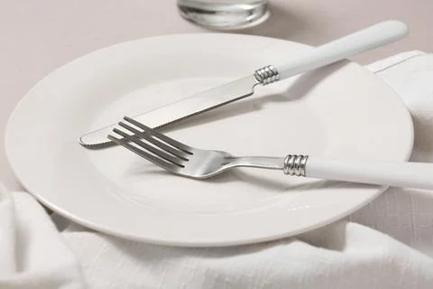 Elegant white ceramic plate with silverware, knife and fork on a minimalist t Stock Photos