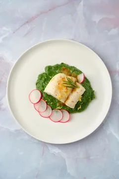 Elegant white cod fish served on vibrant spinach puree with sliced radishes.. 库存照片