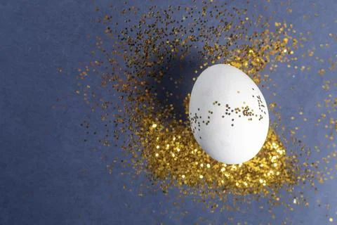 Elegant white Easter egg with gold glitter on a blue background Stock Photos