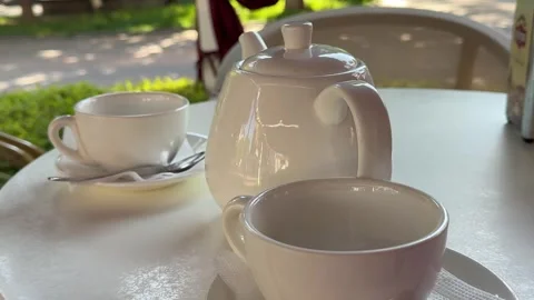 Elegant white tea set on table with white tablecloth in cozy outdoor cafe Stock Footage 345732005