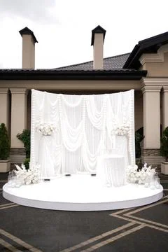 Elegant white wedding backdrop with draped fabric, flowers and pearl garlands Photos