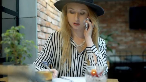 Elegant woman making notes while speaking on cellphone in the cafe Stock-Footage 70658761