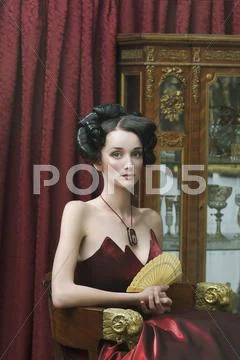 Elegant young woman seated in red ball gown Stock Photos