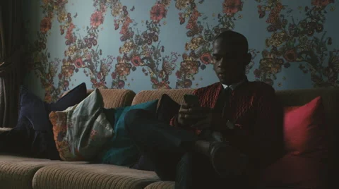 Elegantly Dressed Young Black Man Sitting on Sofa and Typing on Smartphone Stock Footage 59864098