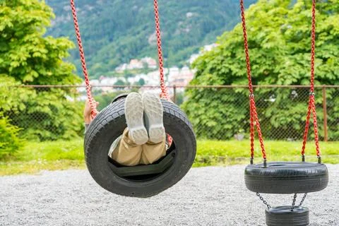 Elementary boy on a tire swing made from chains and car tires in a park. View of Stock Photos