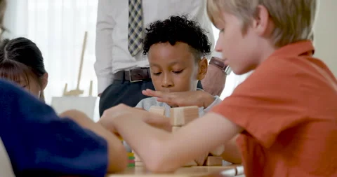 Elementary boys work with colorful blocks at group desk while male teacher Stock Footage 335459945