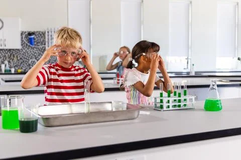 Elementary classmates adjusting goggles while mixing green liquids in test tubes Stock Photos