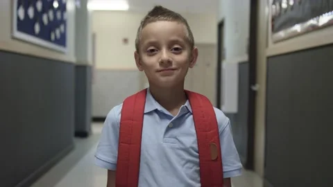 Elementary or Primary school boy with backpack stares at camera in school hall Video stock 140040111