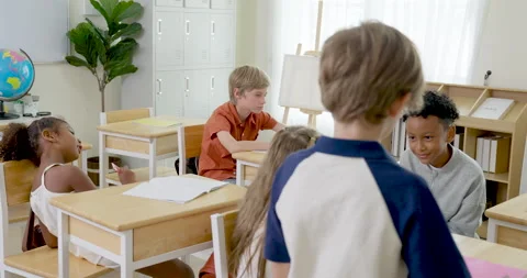 Elementary pupil group shares cheerful peer interaction at wooden desks, Stock Footage 341930366