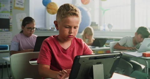 Elementary School Boy Sitting at Desk, Using Digital Tablet, Studying Basic Stock Footage 317169558