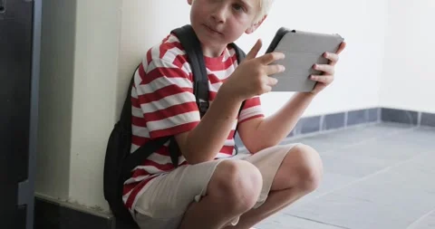 Elementary school boy squatting on tiled entry with backpack, reacting to Stock Footage 339591344