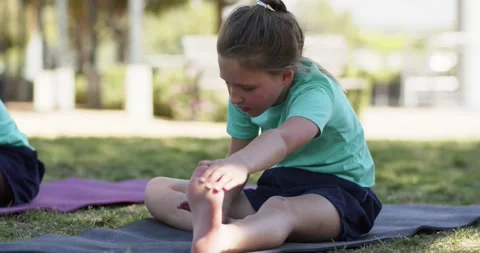 Elementary school girl after cue doing seated forward stretch on dark mat Stock Footage 343099007