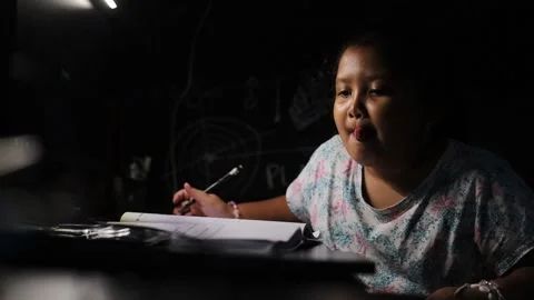 Elementary school girl is doing math homework, sitting at a desk with a book Stockbeeldmateriaal 337562224