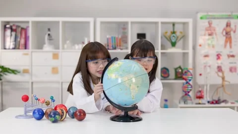 Elementary School Girls in Lab Coats Studying World Globe in Science Classroom Stock Footage 340775386