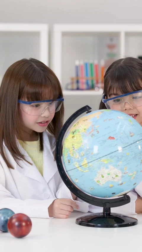 Elementary School Girls in Lab Coats Studying a World Globe Stock Footage 342313310