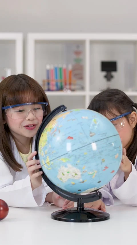 Elementary School Girls in Lab Coats Studying a World Globe Stock Footage 344943904