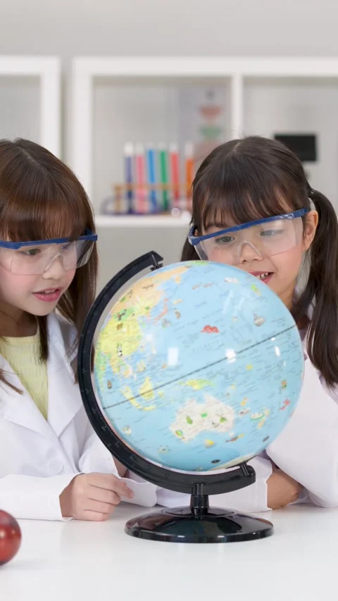 Elementary School Girls in Lab Coats Studying World Globe in Science Classroom Stock Footage 346453063