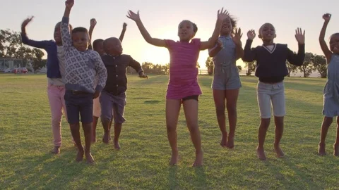 Elementary school kids jumping outdoors at sunset Stock Footage
