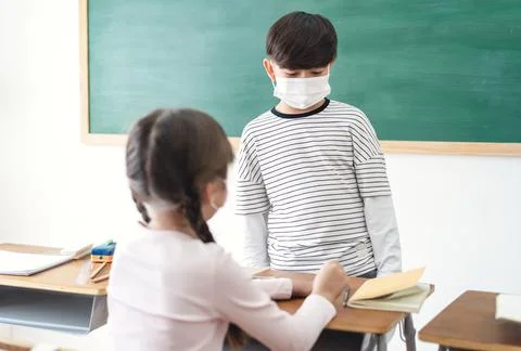 Elementary school kids wearing medical face masks talking during lesson in class Stock Photos