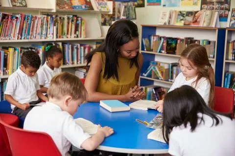 Elementary School Pupils Reading In Library With Teacher Stock Photos