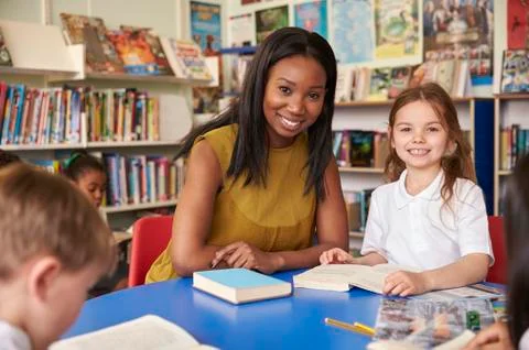 Elementary School Pupils Reading In Library With Teacher Stock Photos