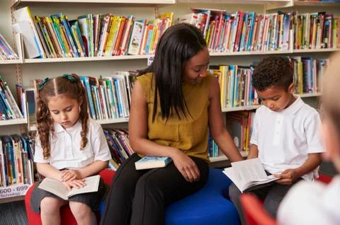 Elementary School Pupils Reading In Library With Teacher Stock Photos