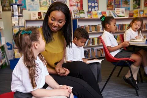 Elementary School Pupils Reading In Library With Teacher Stock Photos