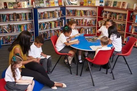 Elementary School Pupils Reading In Library With Teacher Stock Photos