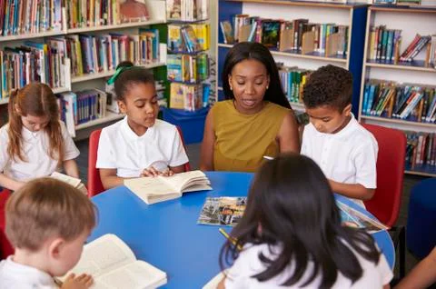 Elementary School Pupils Reading In Library With Teacher Stock Photos