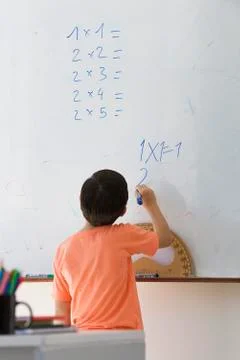 Elementary school student doing math equation on whiteboard, rear view Foto stock