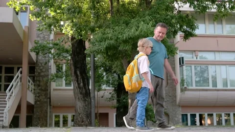 Elementary school student walks from school accompanied by father Stock Footage 233905247