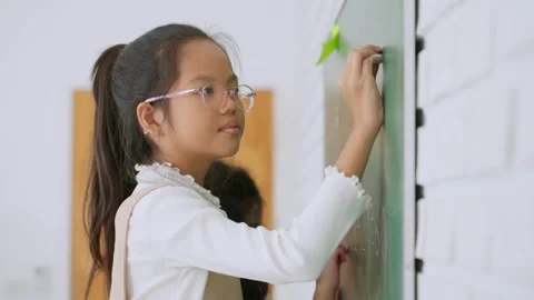 Elementary school student writing answer on a chalkboard in classroom at school. Stock Footage 249832733