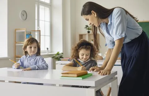 Elementary school students sit at desks and write or draw under the supervision Fotos Stock