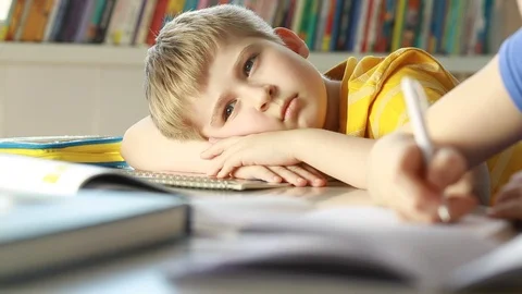  Elementary schoolboy looking tired and exhausted resting his head on desk in cl Stock Footage 87611571