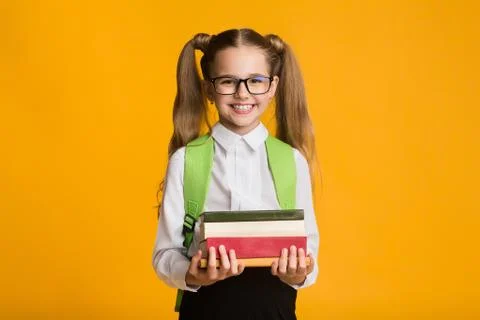 Elementary Student Girl Holding Stack Of Books Over Yellow Background Stock Photos