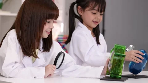 Elementary Students in Lab Coats Examining Cell Models with Magnifying Glass Stock Footage 342577572