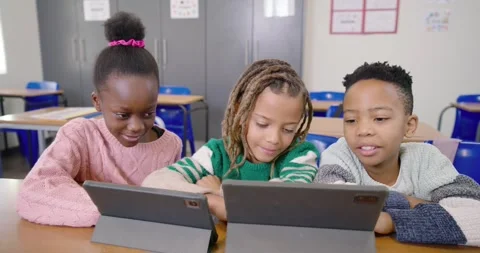 Elementary students noticing two tablets, tapping and leaning on desk, Stock Footage 340631390