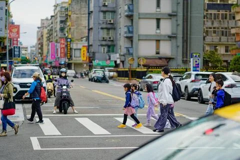 Elementary teacher leading students over crosswalk, motorcyclist in backgroun Foto stock