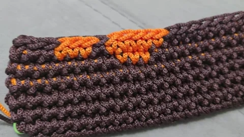 Elements of a bag crocheted from brown and orange cord. On a wooden base. Stock Footage 313859863
