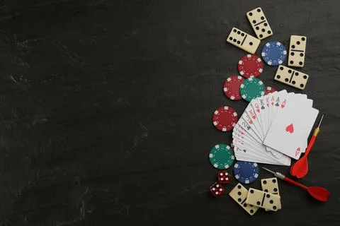 Elements of different board games on black slate table, flat lay. Space for t Stock Photos