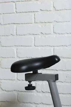 Elements of an exercise bike. Saddle on the background of a white brick wal.. Stock Photos